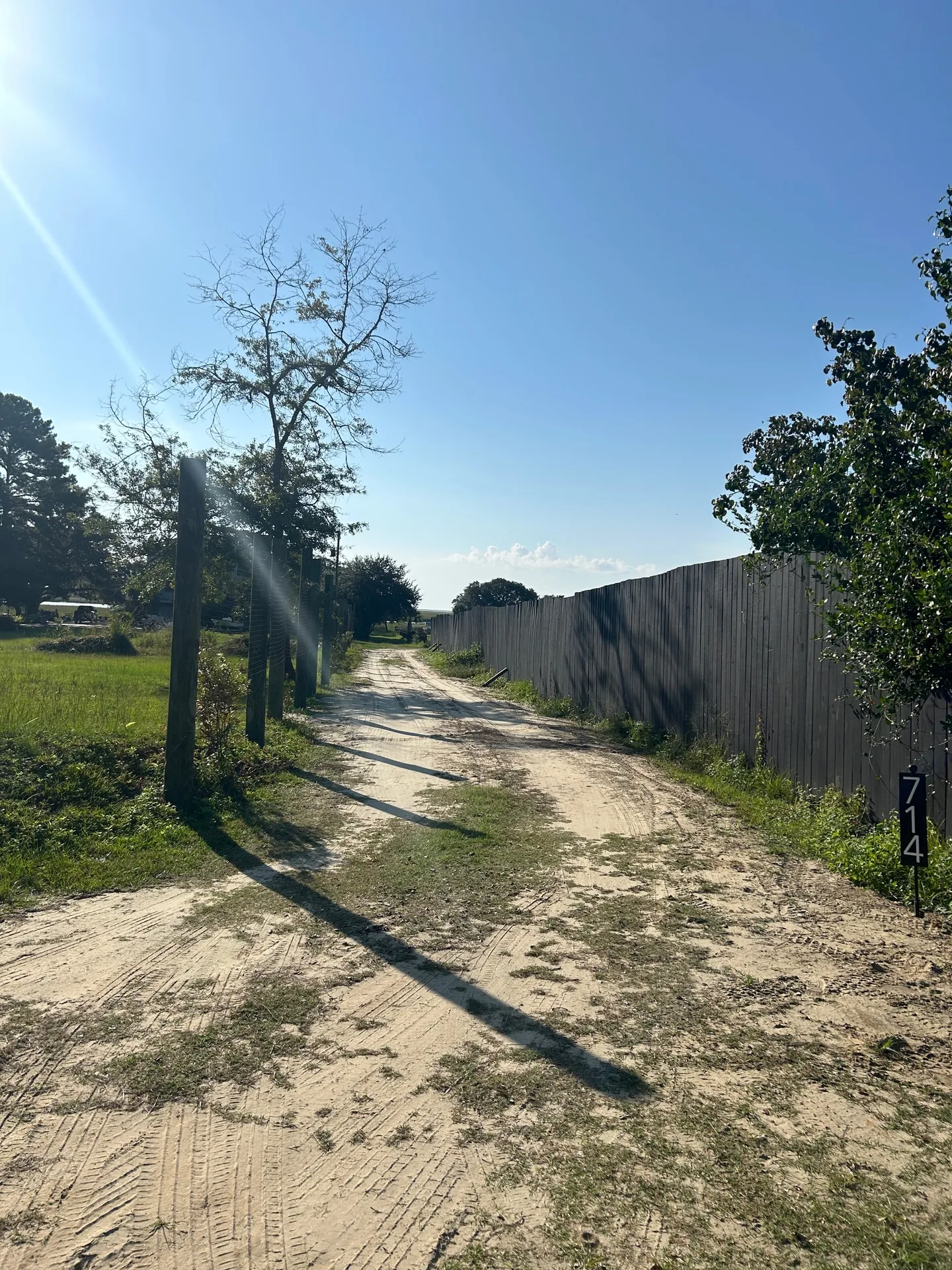 Long sandy driveway with address marker 714 and weathered privacy fence