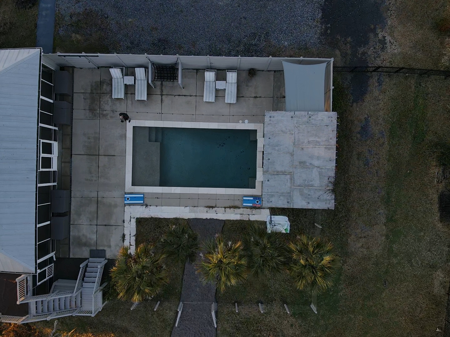 Top-down drone view of rectangular pool, deck, loungers, and pool house