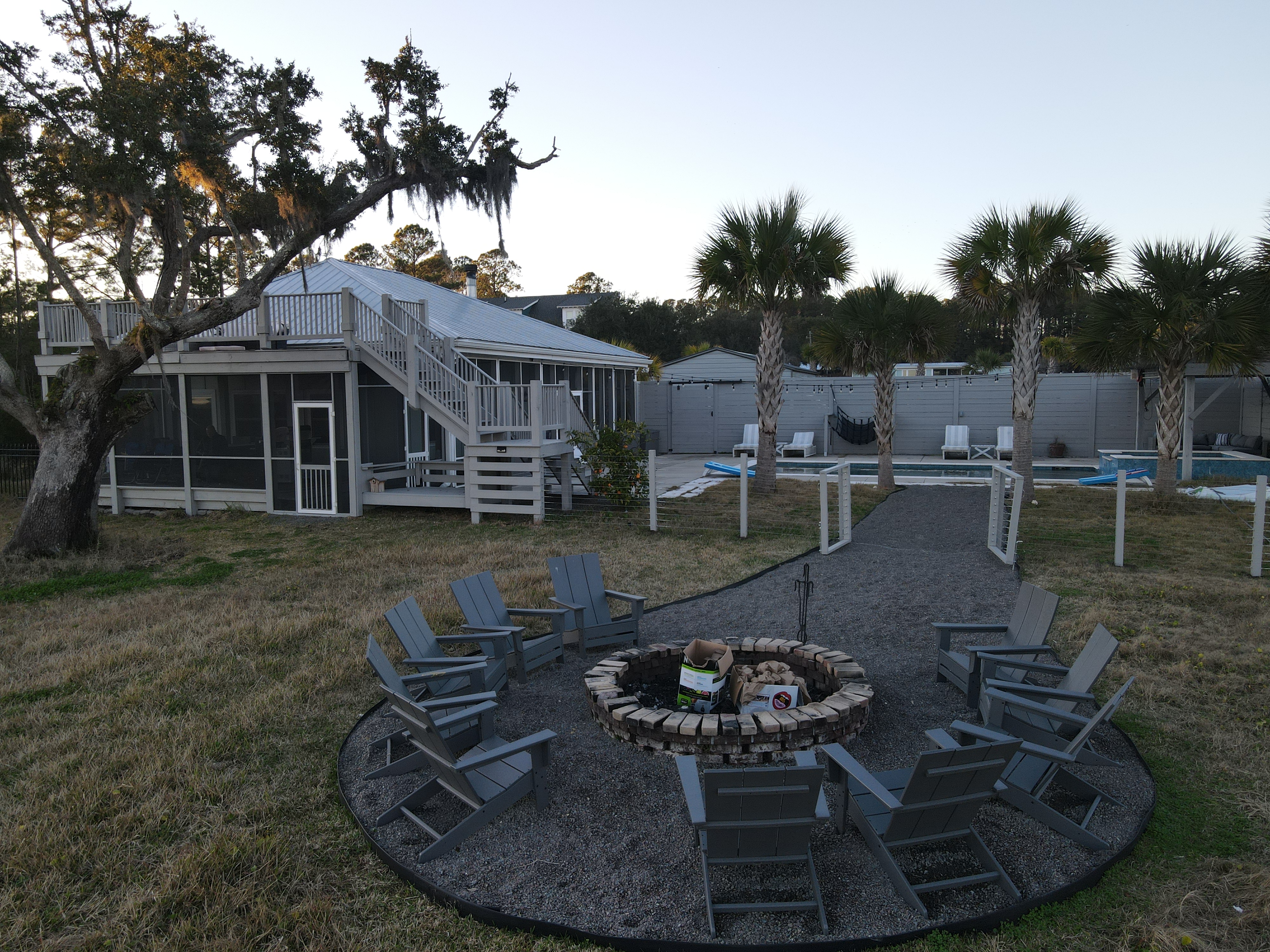 Dusk view of compound — fire pit, raised pool house, palmettos, and screened porch