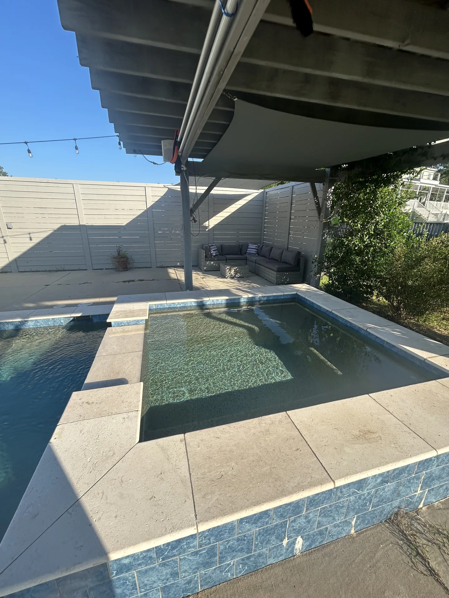 Pool and spa area through the gray pergola with wicker sectional and navy pillows