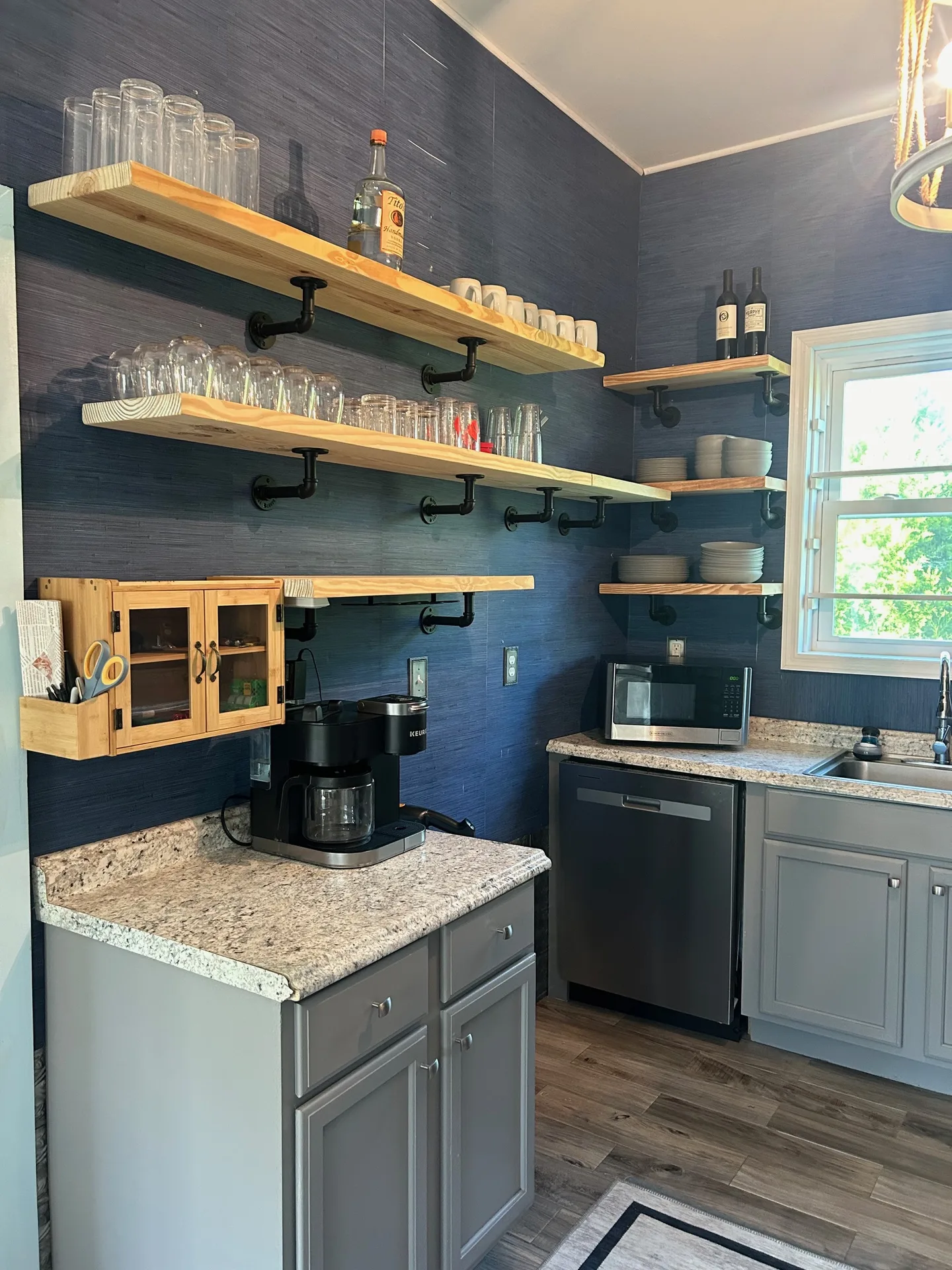 Bar area with navy walls, live-edge shelves, industrial pipe brackets, and extensive glassware