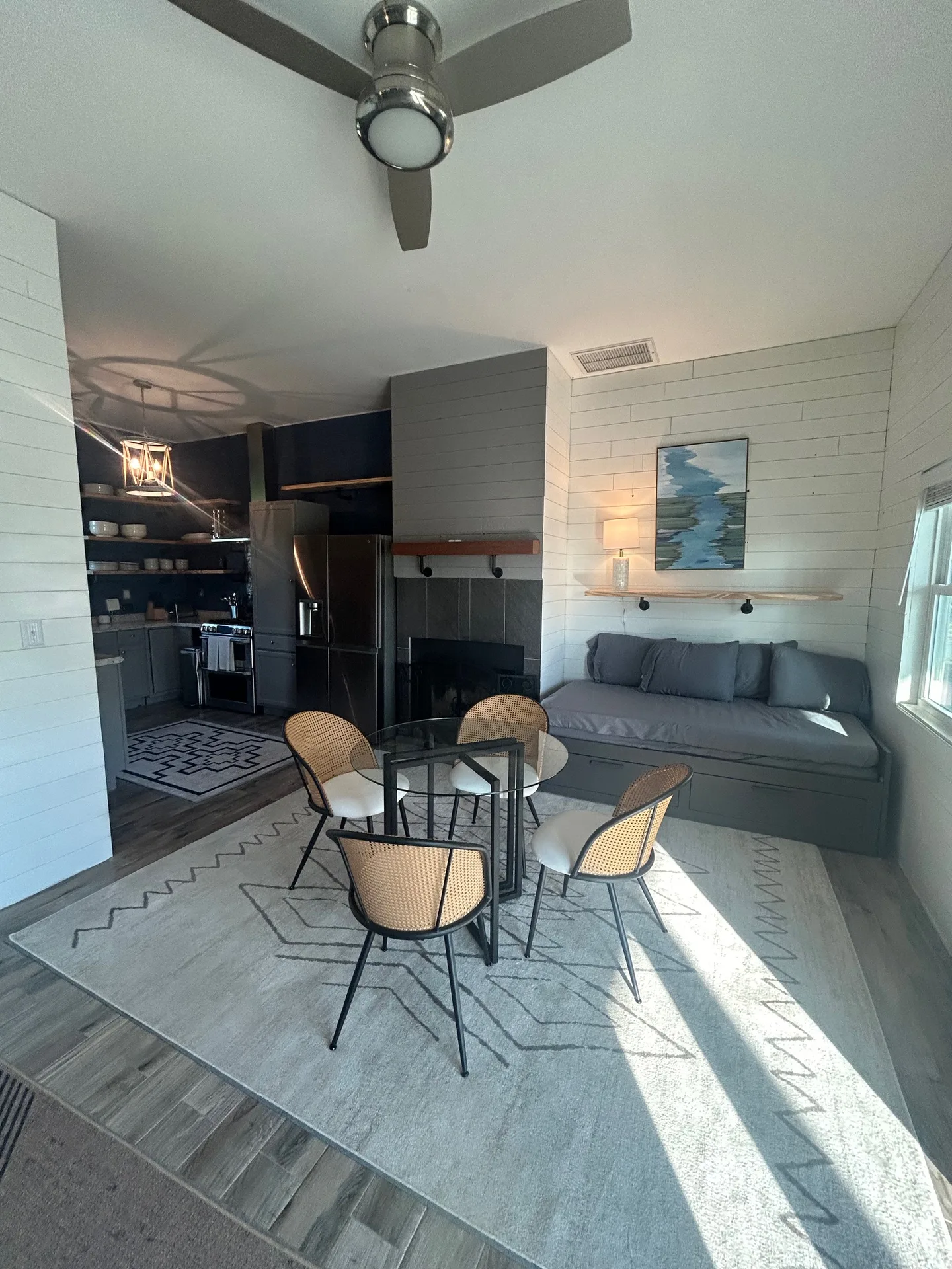 Open-concept living with glass dining table, cane-back chairs, navy kitchen, and stone fireplace