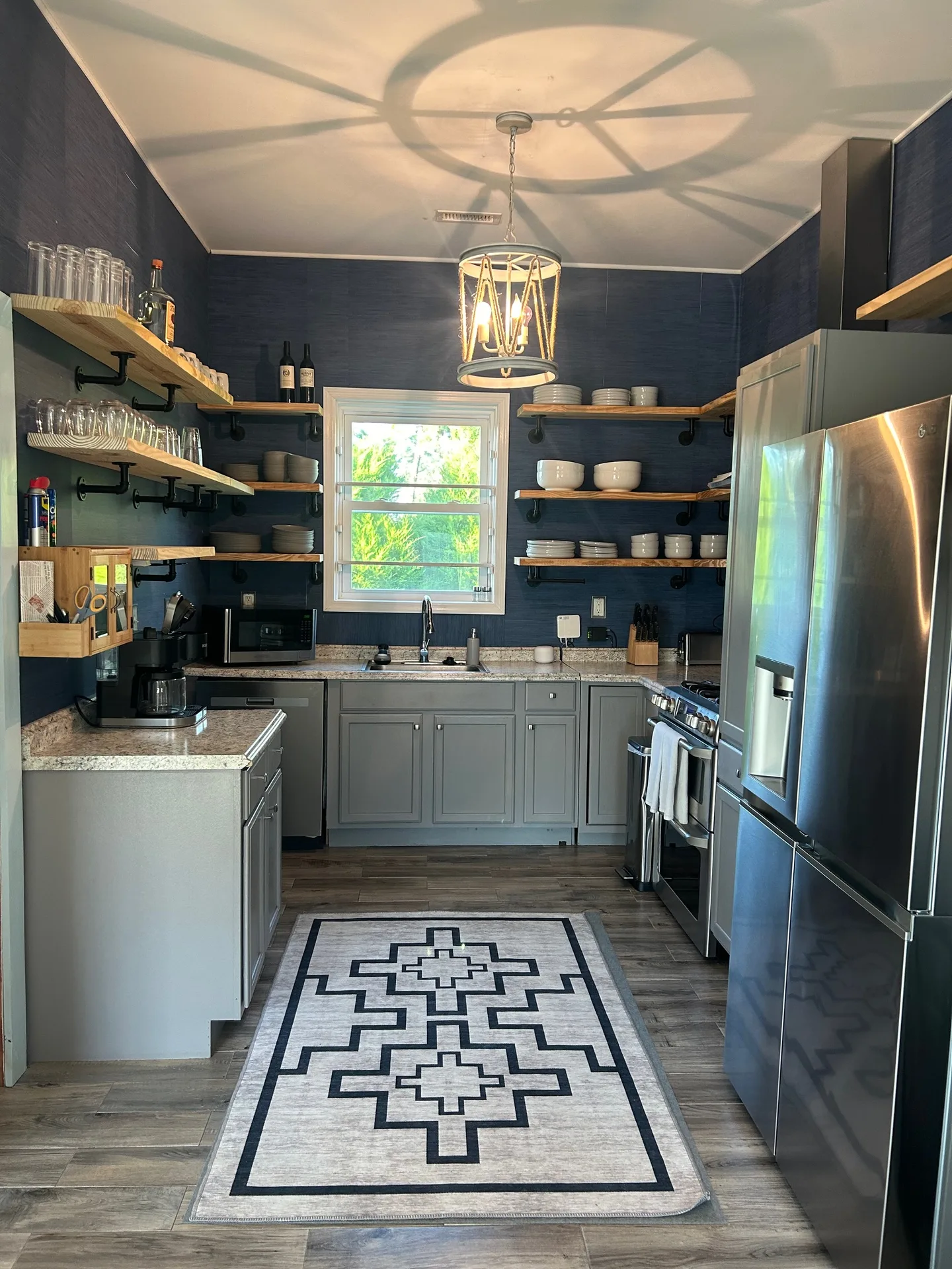 Galley kitchen with navy grasscloth walls, live-edge shelves, and geometric pendant shadow