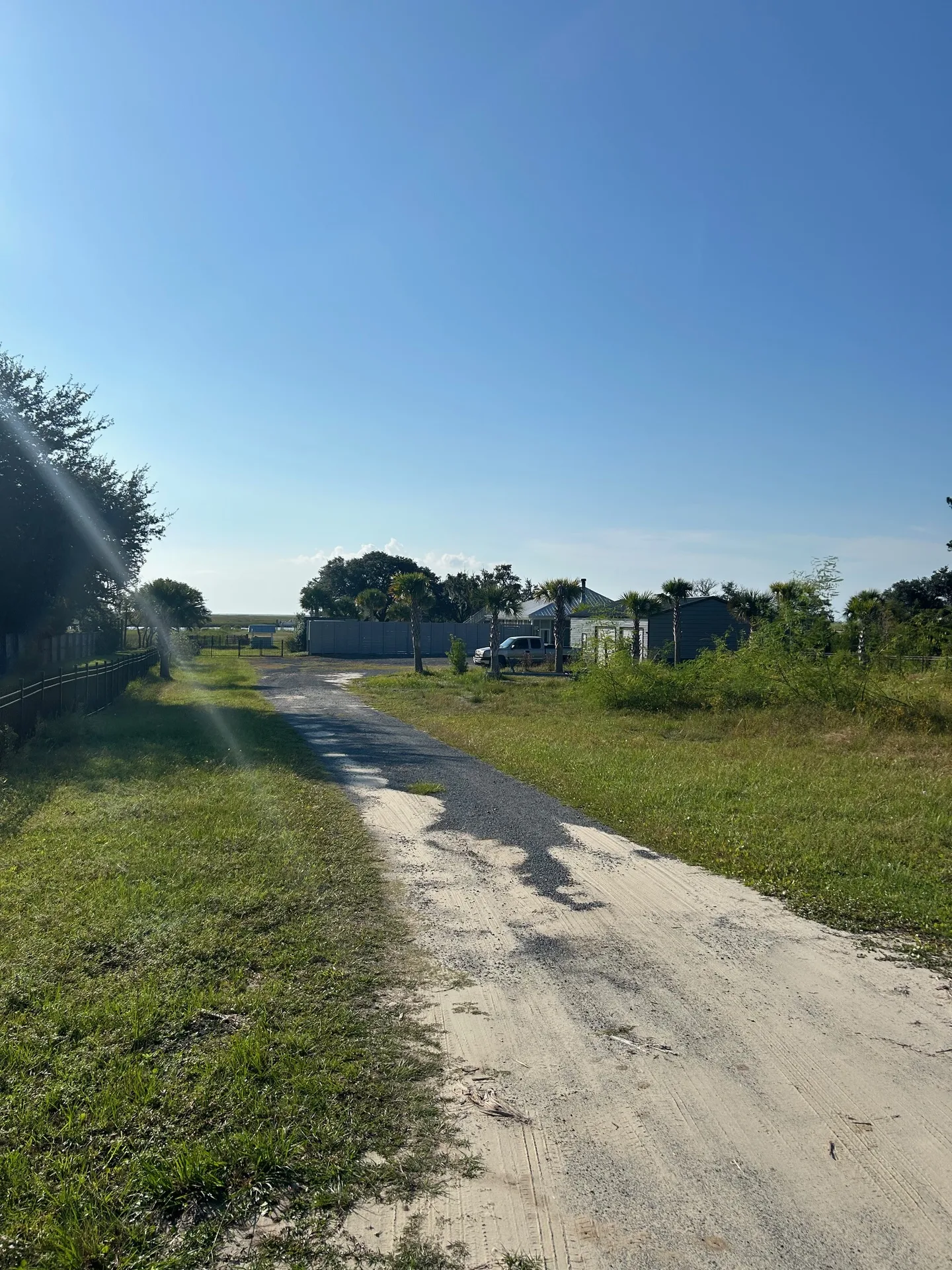 Sandy driveway curving through property with palmettos and compound buildings