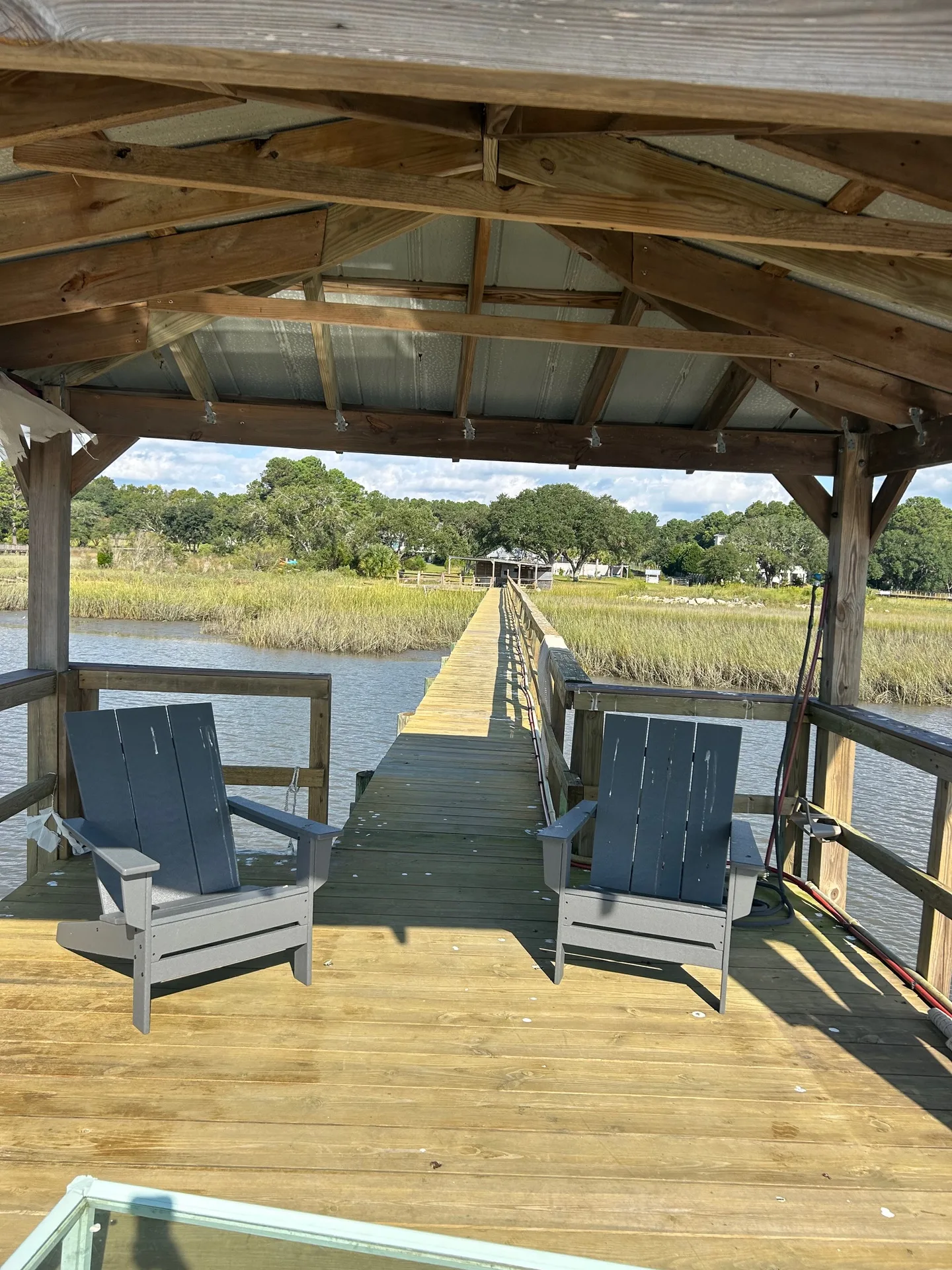 Covered dock looking back along the long pier to shore with string lights and fishing rod