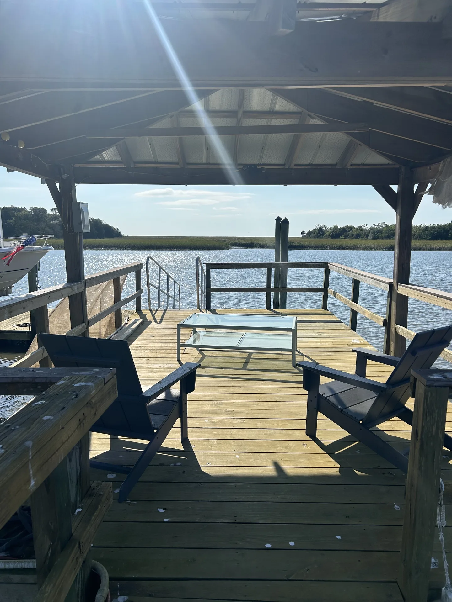 Covered dock with Adirondack chairs, glass coffee table, swim ladder, and moored boat on Graham Creek