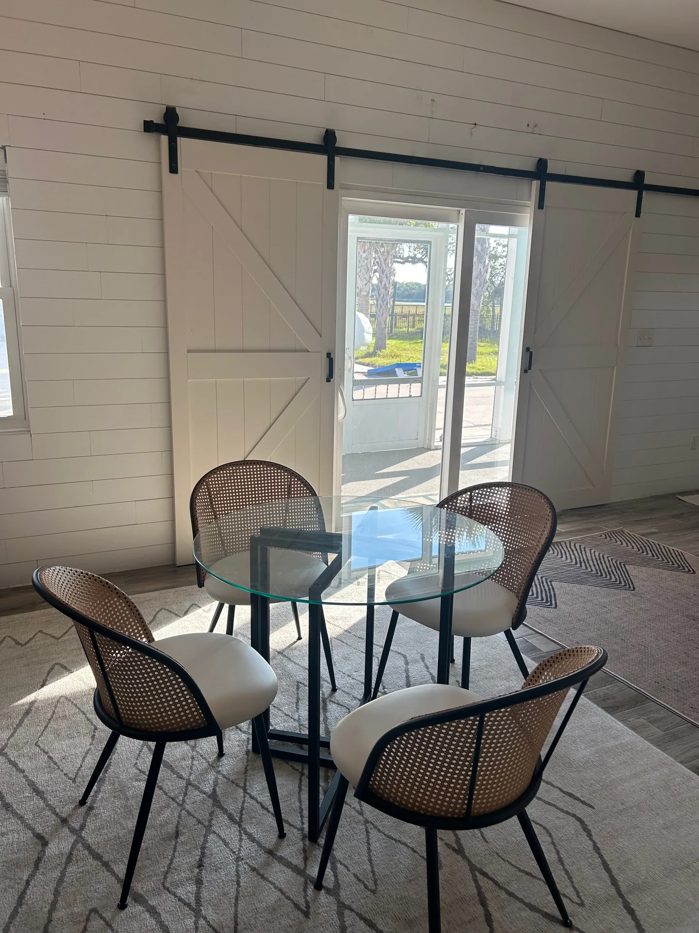 Dining nook with glass table, cane-back chairs, and white barn doors on sliding track to deck